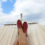 Feet resting on a hammock with red sneakers, epitomizing summer relaxation and leisure outdoors.